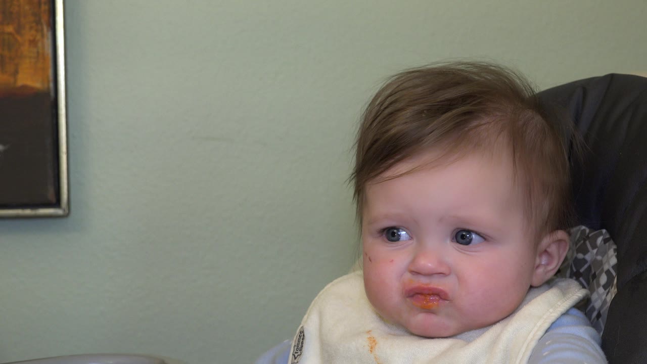 In Westminster, Colorado, the toddler sits in the high chair and looks off to the side, with orange food visible on the lips and bib.