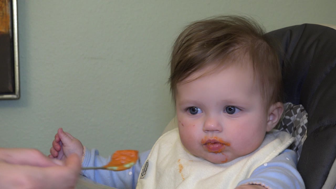 In Westminster, Colorado, the child looks ahead with orange food on the lips while the adult-held spoon waits just below the face.