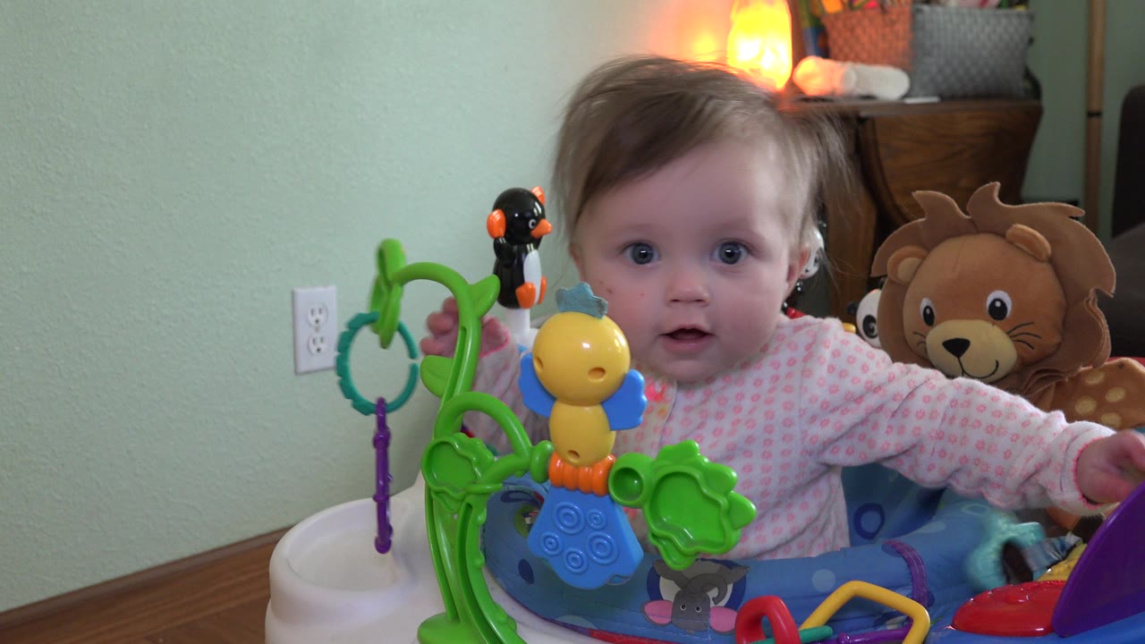 Baby in a walker facing the camera with colorful toys in front.