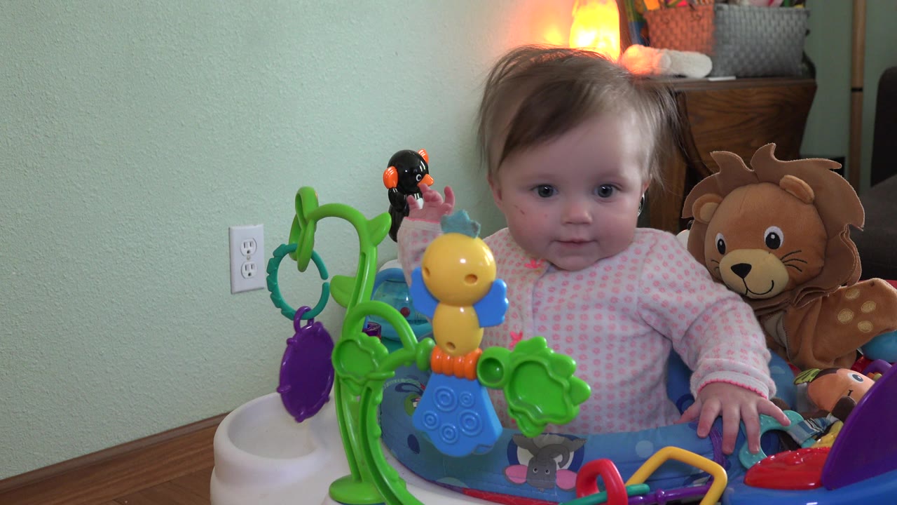 Baby girl seated in a play station with colorful toys.