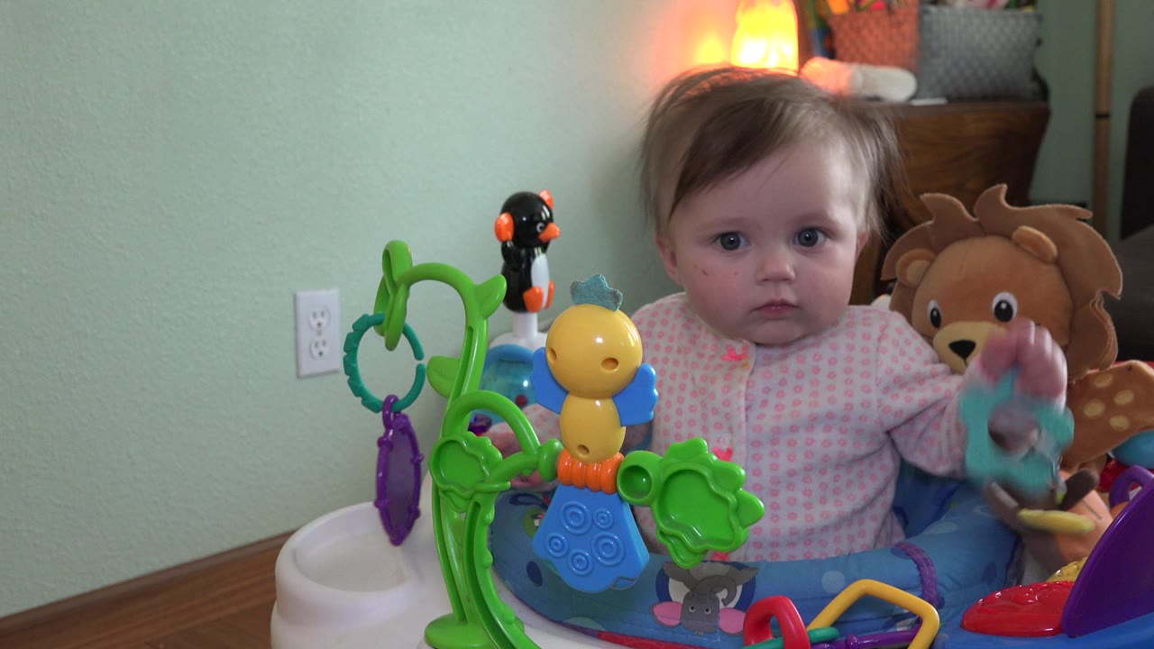 Baby seated among colorful toys in a home interior.