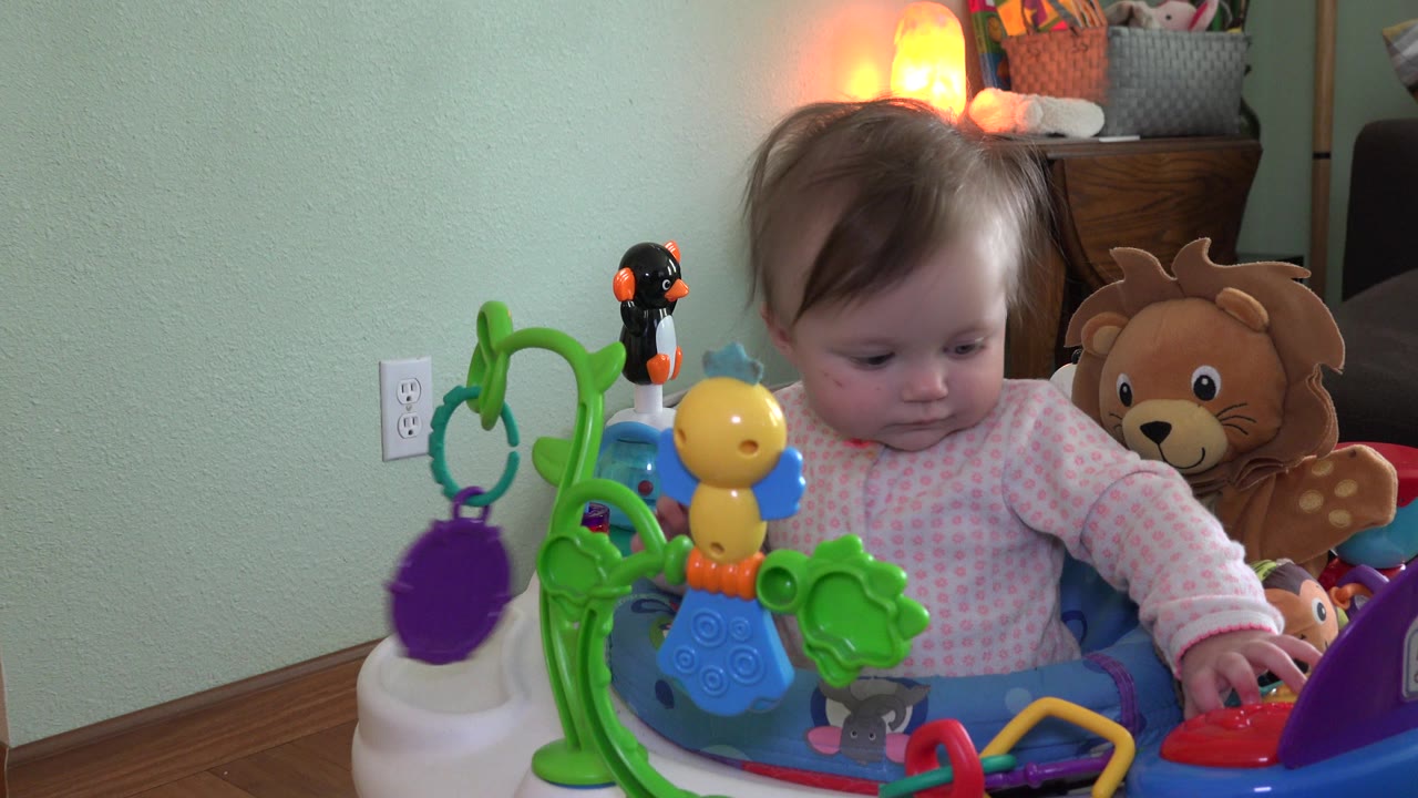 Baby sitting in a colorful toy activity cart indoors.