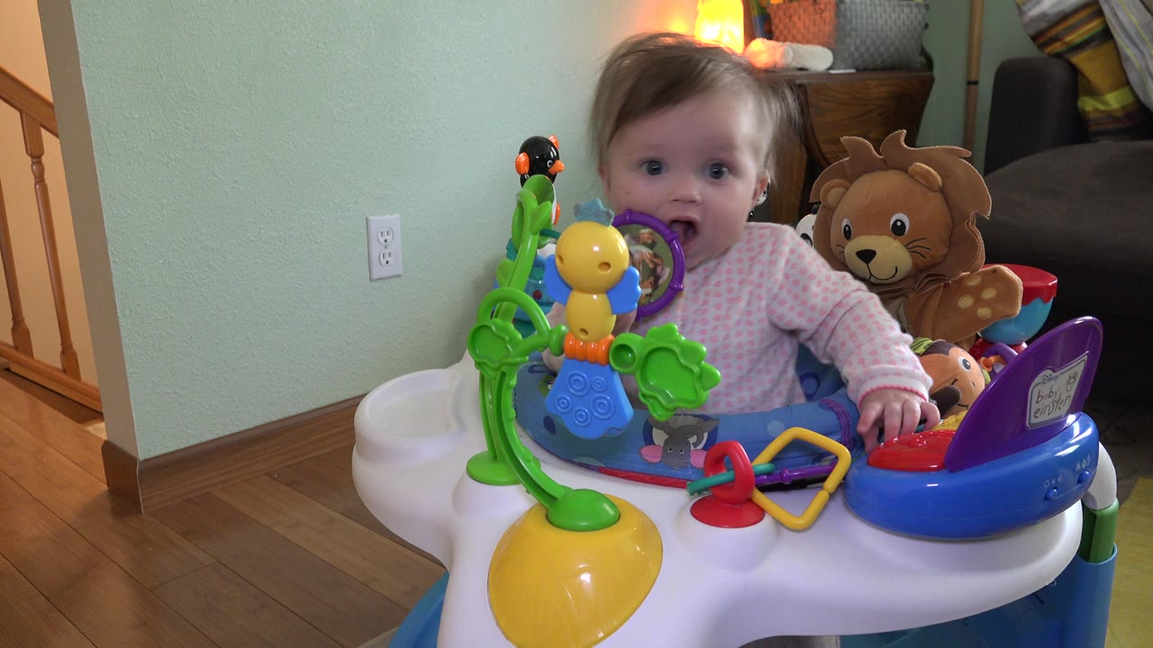 Toddler seated in a colorful activity chair with toys.