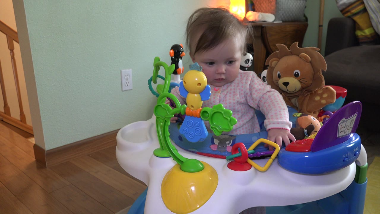 Baby standing in an activity table filled with colorful toys.