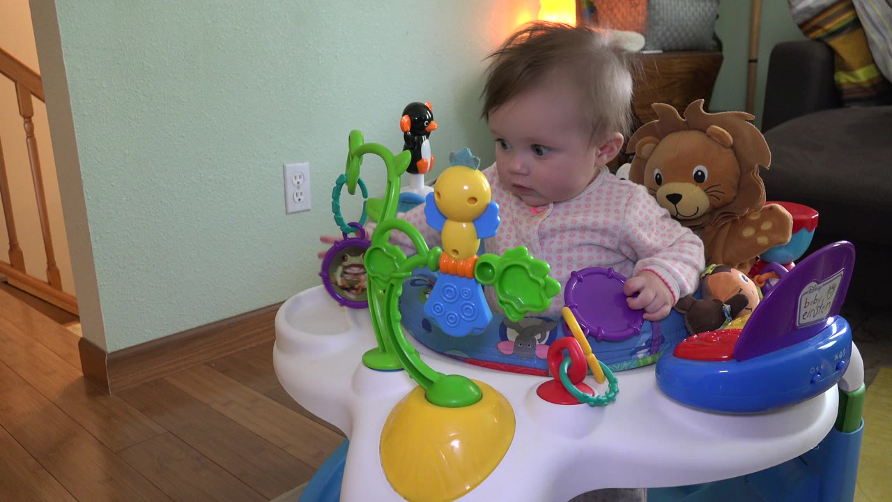 Baby girl in a toy-filled baby walker inside a living room.