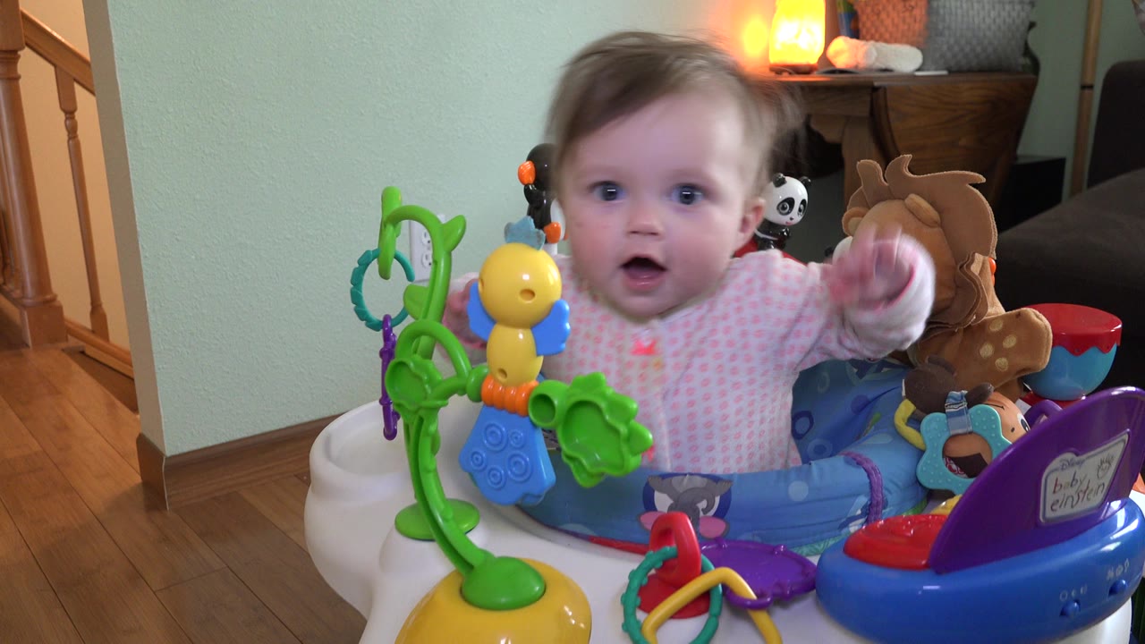 Baby in a colorful activity jumper reaching toward the camera.