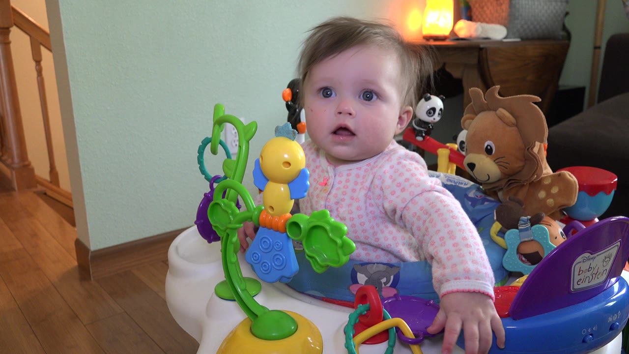 Baby seated in a colorful activity center indoors.