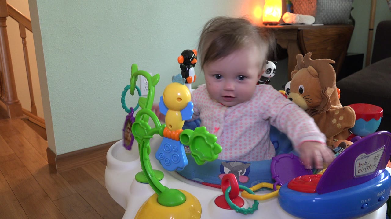 Infant in a colorful baby walker facing the camera indoors.