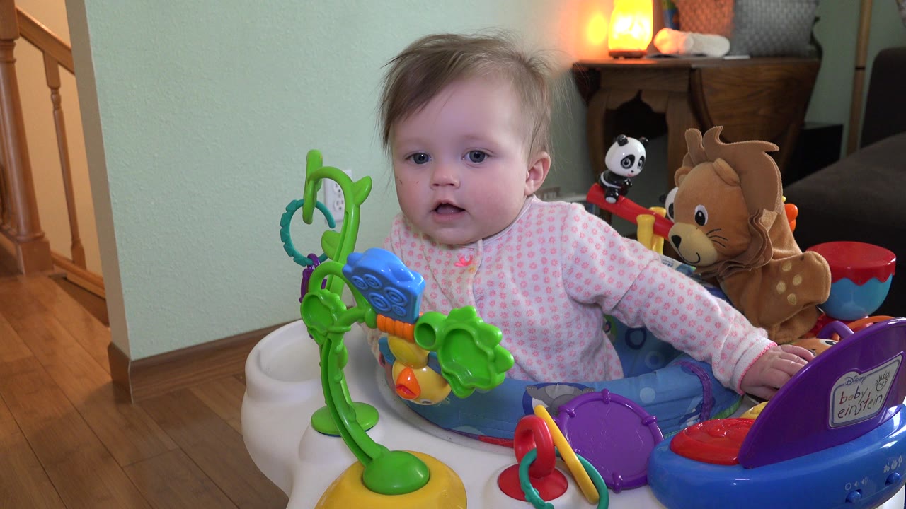 Infant sitting in a colorful activity walker inside a home.