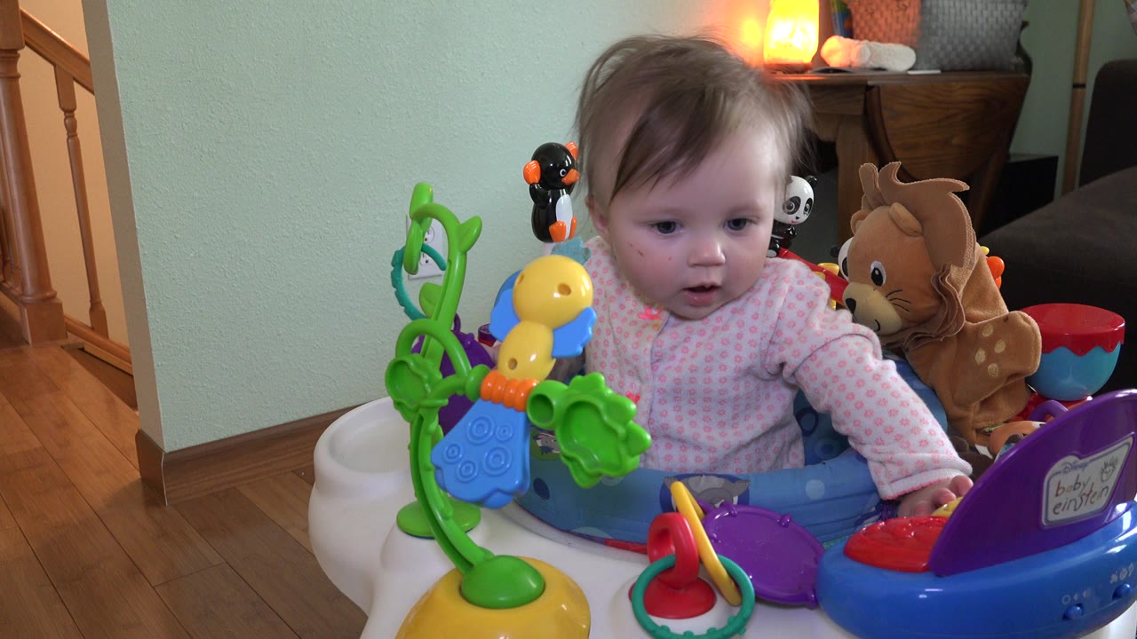 At 0:00, a baby sits in a blue activity chair in a Westminster, Colorado home interior, with green and yellow toys in front and a staircase along the left side.