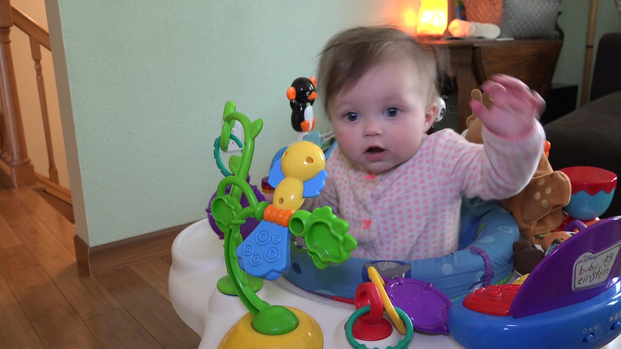 Baby in an activity walker with colorful toys indoors.