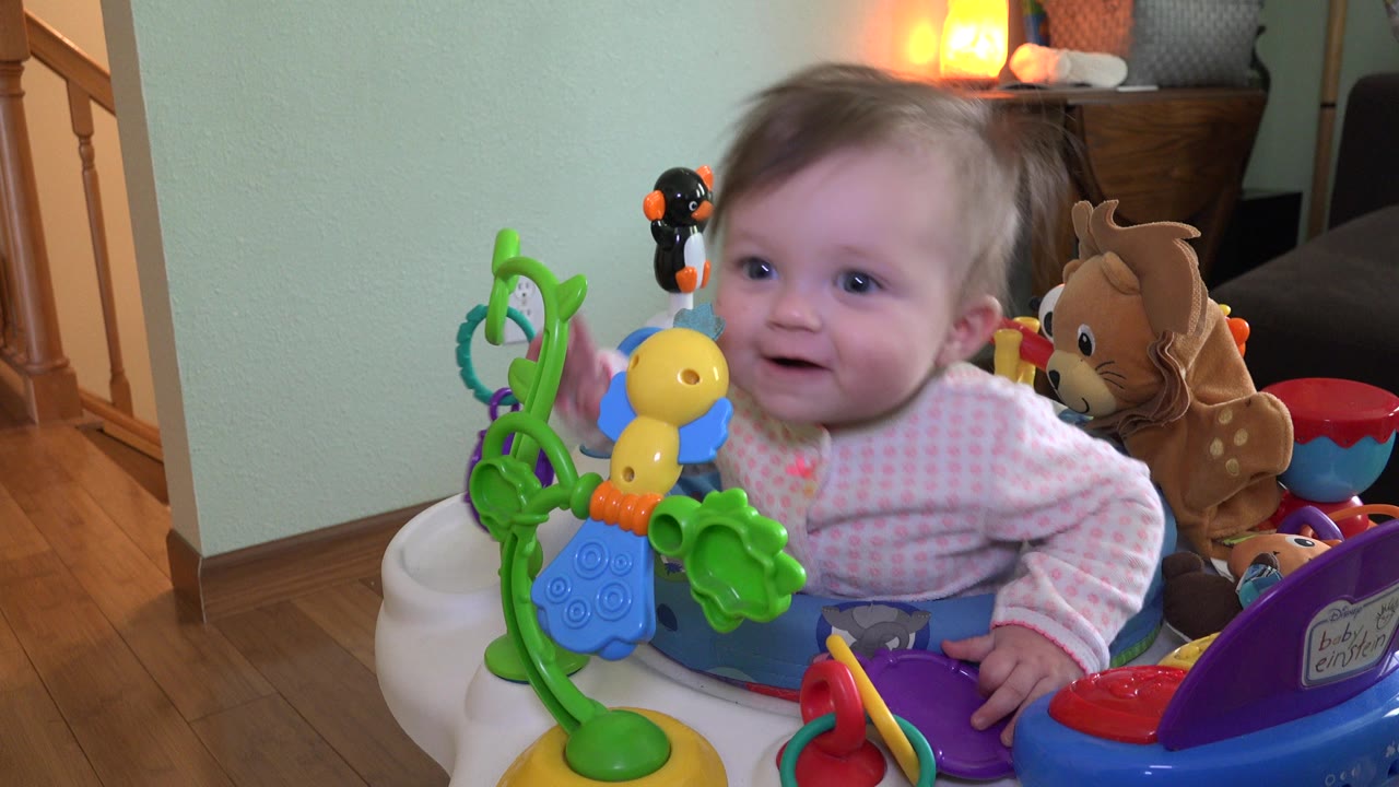 Baby smiling in a blue activity stroller with colorful toys.