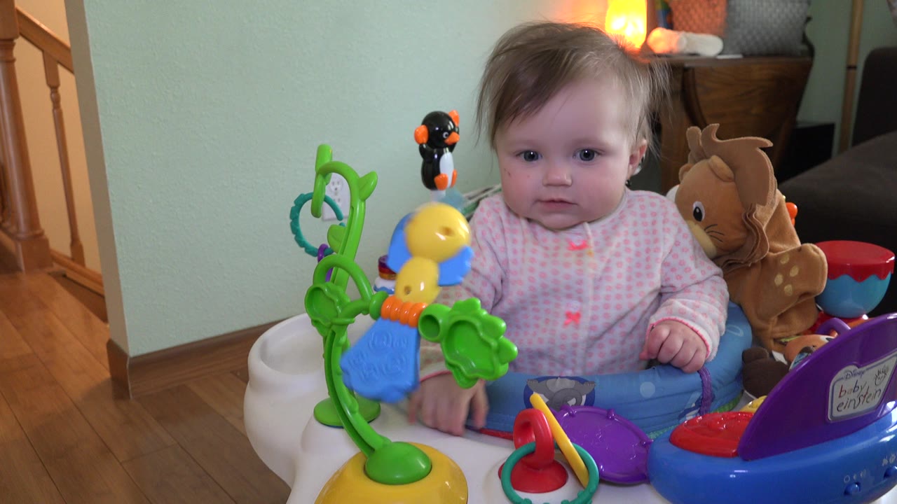 The child remains centered in the Westminster, Colorado home, partly framed by a yellow toy and green play structure on the activity chair tray.