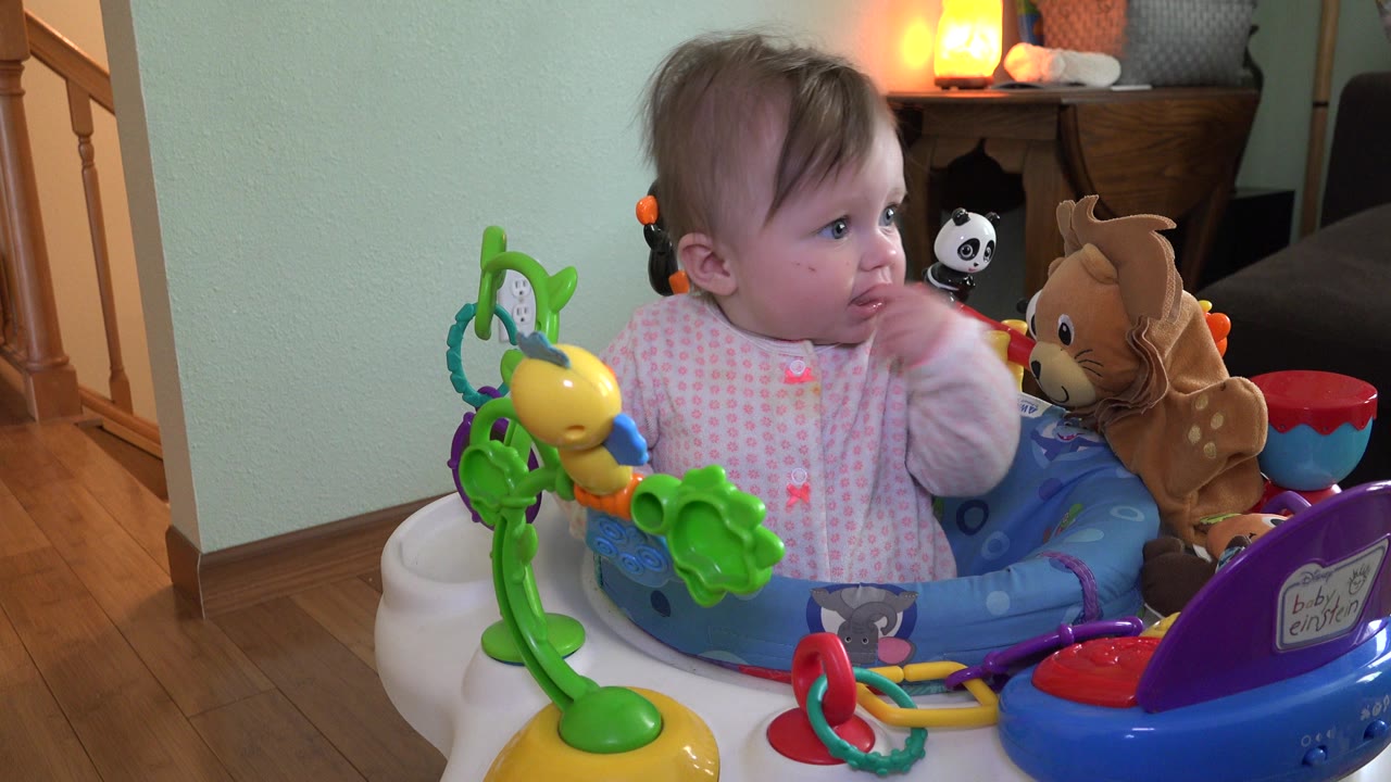 Baby girl in a toy walker looking left inside a home.