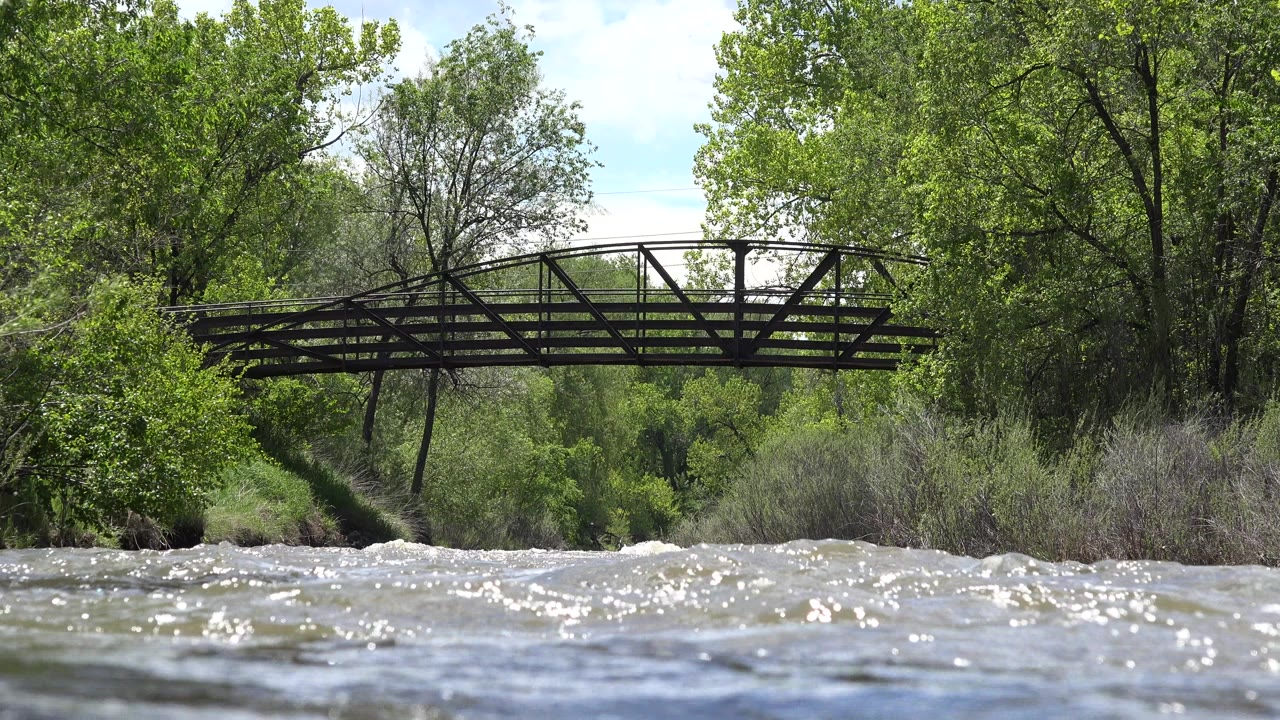 Choppy river below a metal pedestrian bridge and green trees