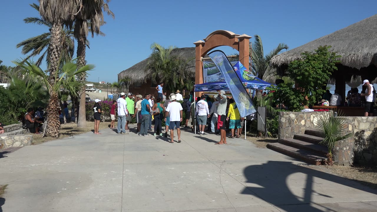 Adults gather near a shaded kiosk as a child runs across pavement.