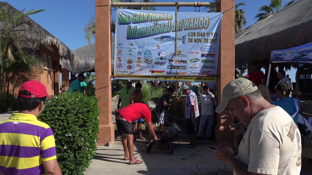 People gathered outside a thatched-roof entrance under a large Spanish tournament banner.