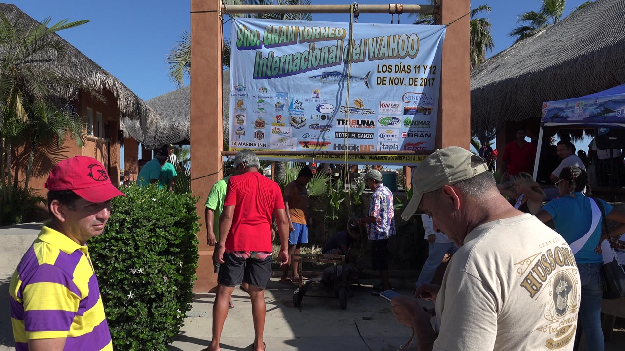 People wait near a large wahoo tournament banner outside a thatched entrance.