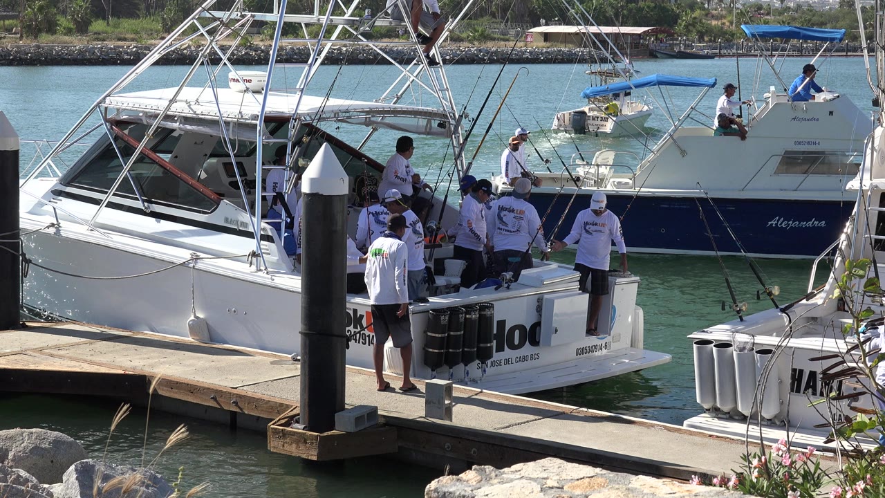 Men stand around a docked white fishing boat beside marina pilings.