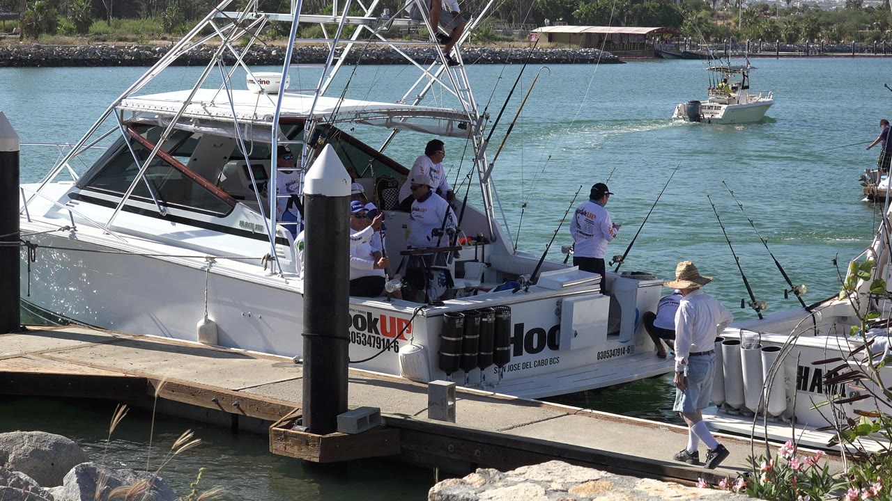 Man walking on a dock beside a white fishing boat with crew aboard.