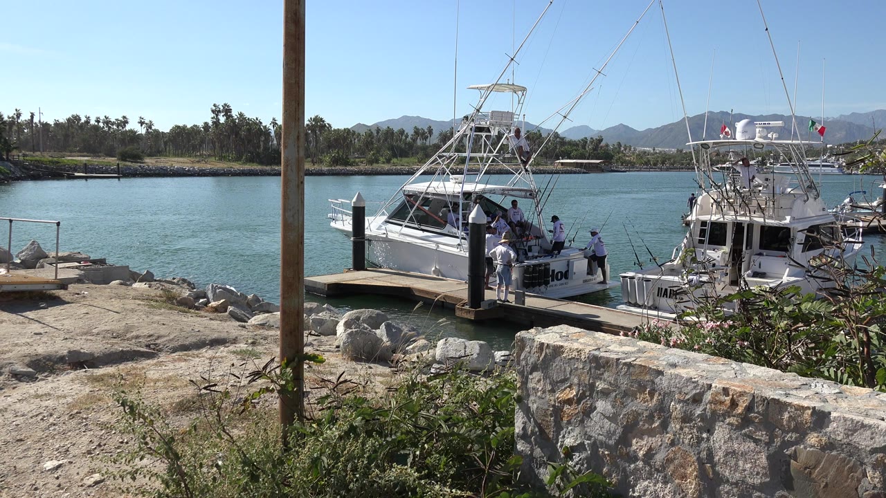 Two white fishing boats at a dock with people on board and along the pier.