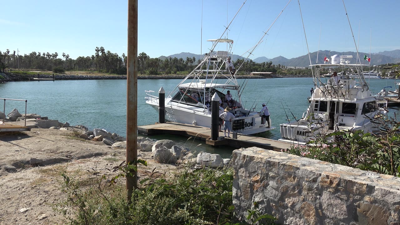 Two white fishing boats moored beside a small dock with people nearby.