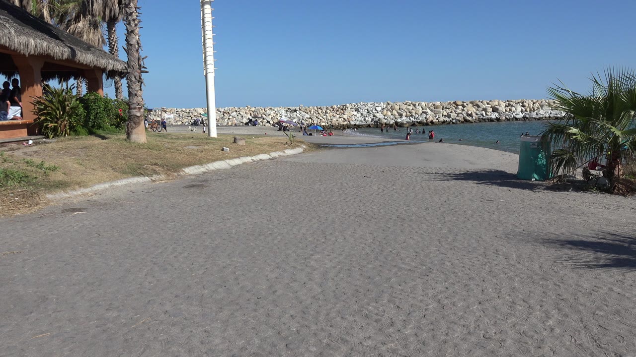 Sandy beach path leading to water and a stone breakwater.