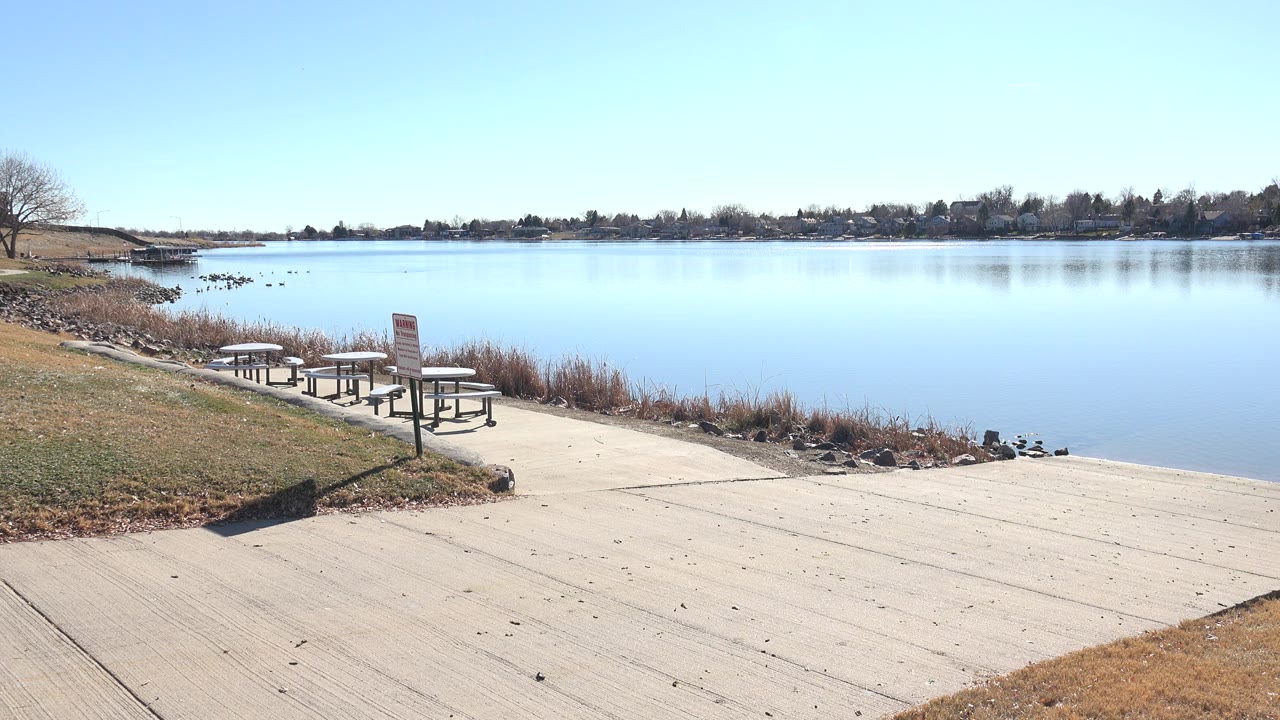 Boat ramp beside a calm lake with picnic tables and shoreline grasses.