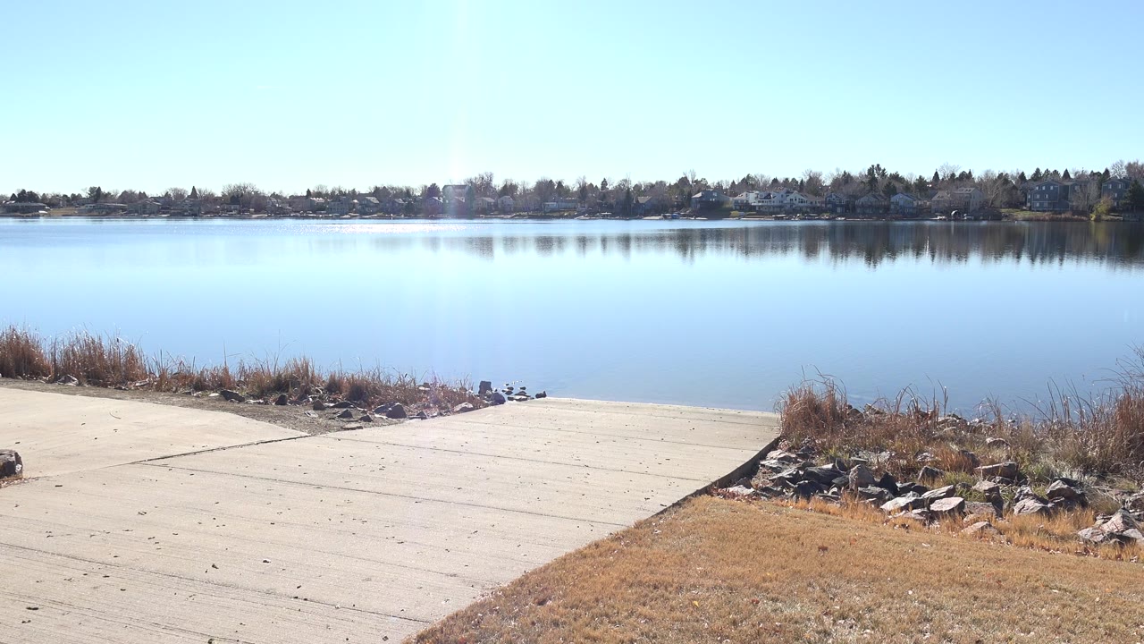 Concrete ramp leading to a calm lake with reeds and rocks at the shore.
