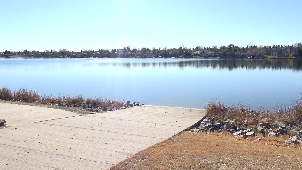 Concrete boat ramp leading to a calm lake with reeds and distant trees.