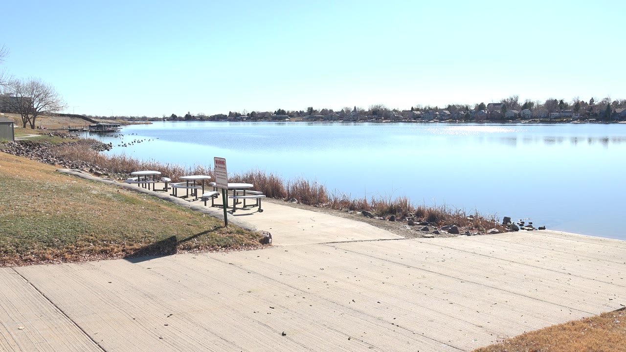 Concrete lakeside ramp with picnic tables beside calm blue water.