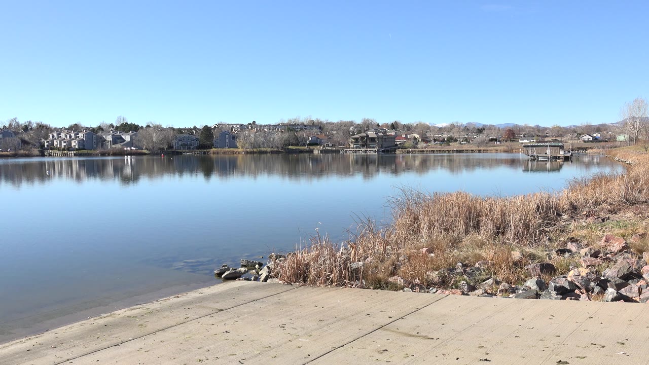 Calm lake beside a concrete shoreline ramp with reeds and rocks.