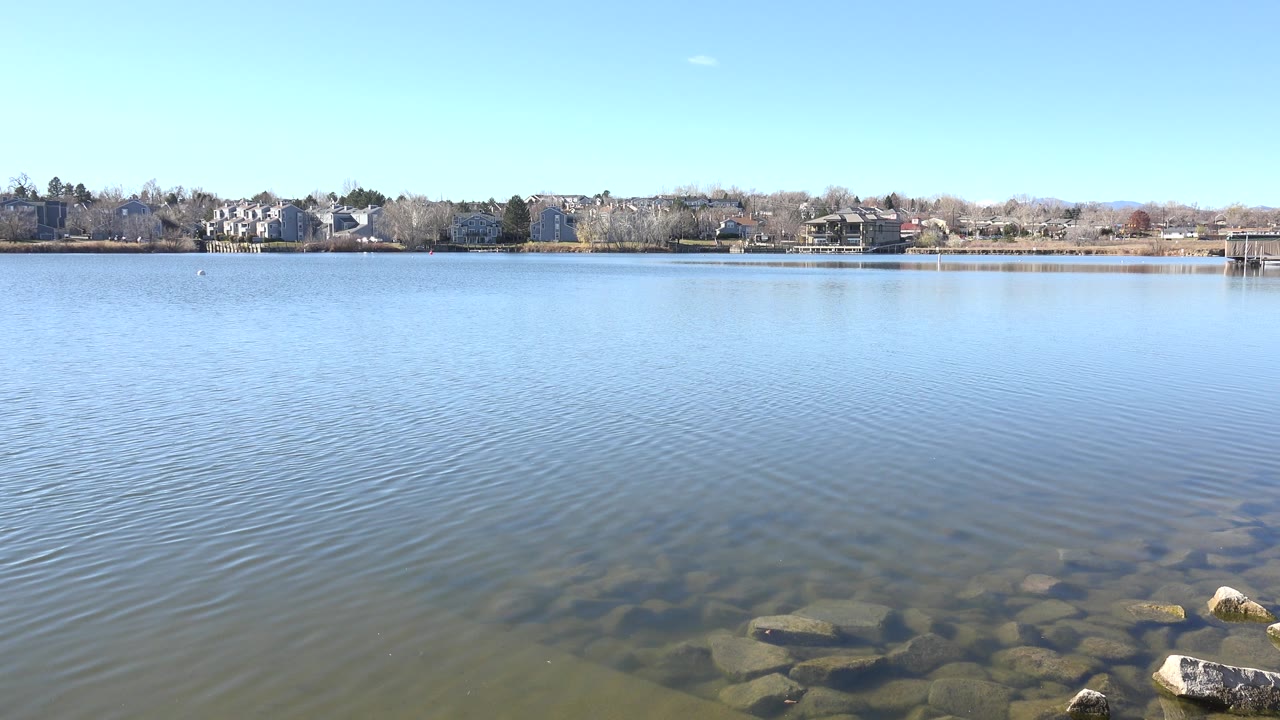 Calm lake water with shoreline rocks and distant houses