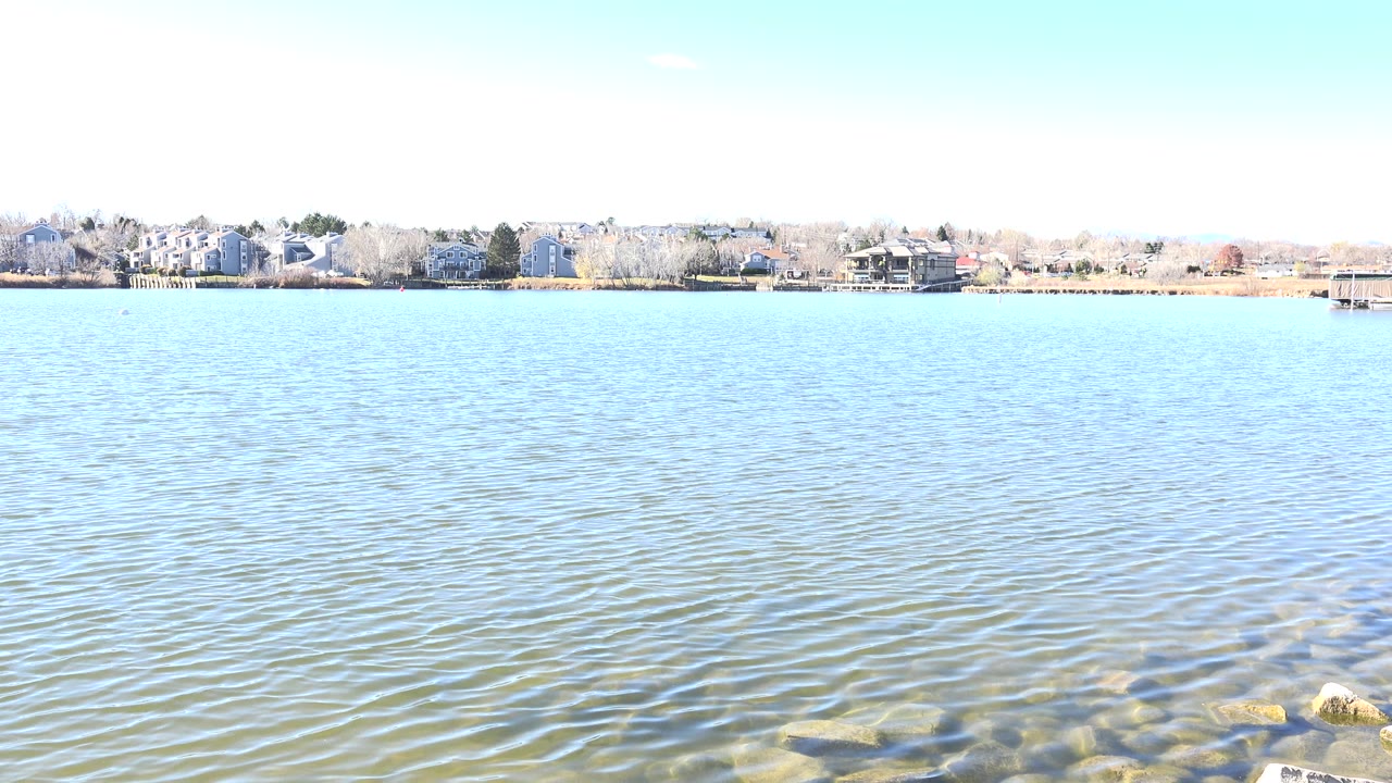 Bright lake water with a distant shoreline and rocks at the lower edge.