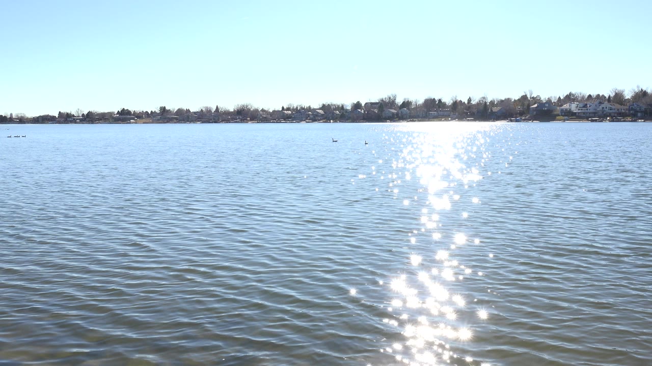 Blue lake water with bright sun reflection and distant shoreline