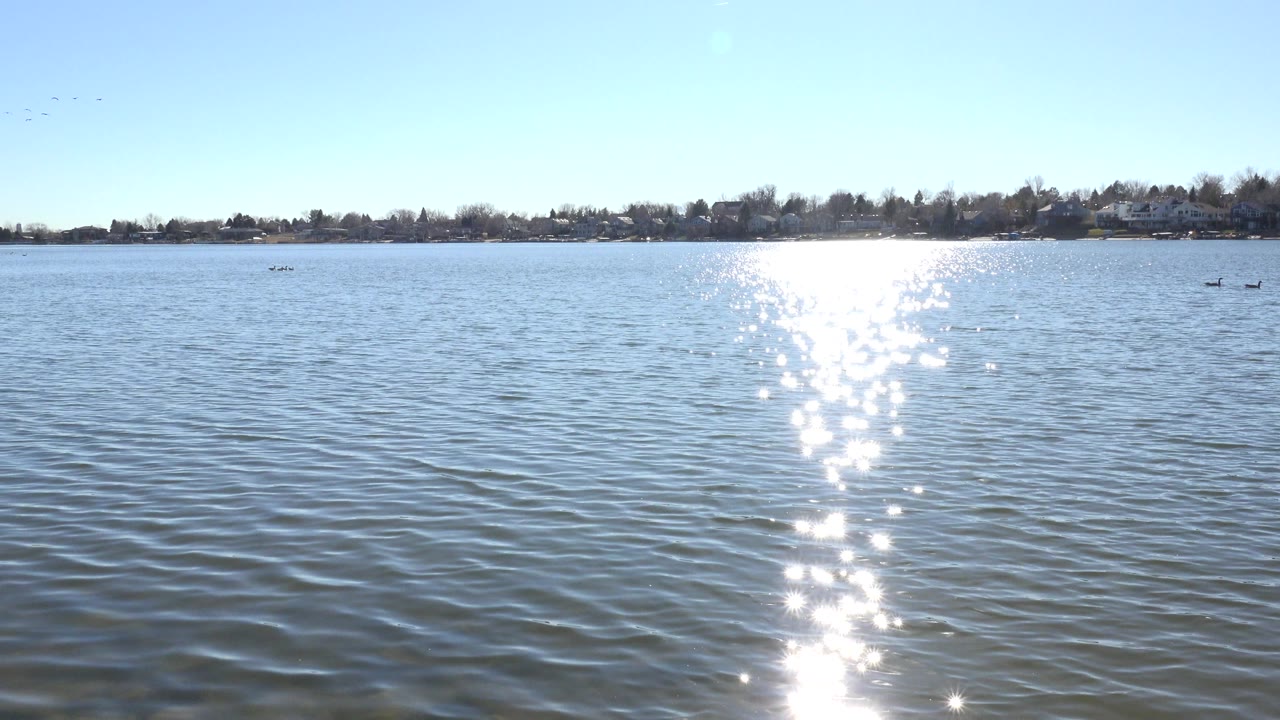 Sunlight glittering on rippled lake water with a distant shoreline.