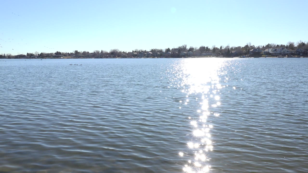 Bright sun reflection on rippled lake water with distant shoreline.