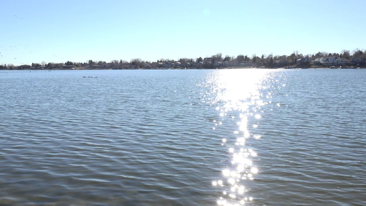 At 0:01, Hidden Lake fills the frame with tight ripples, the glare path sits slightly left of center, the far shoreline remains low on the horizon, and no visible people appear.