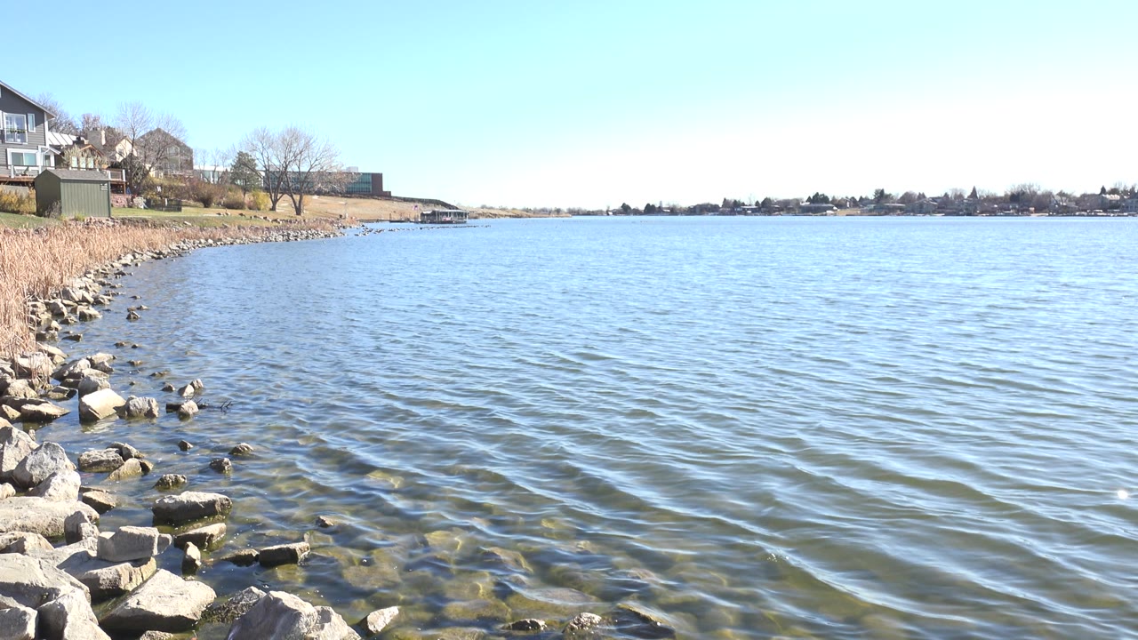 Wide lake surface with rocky bank and houses on the left
