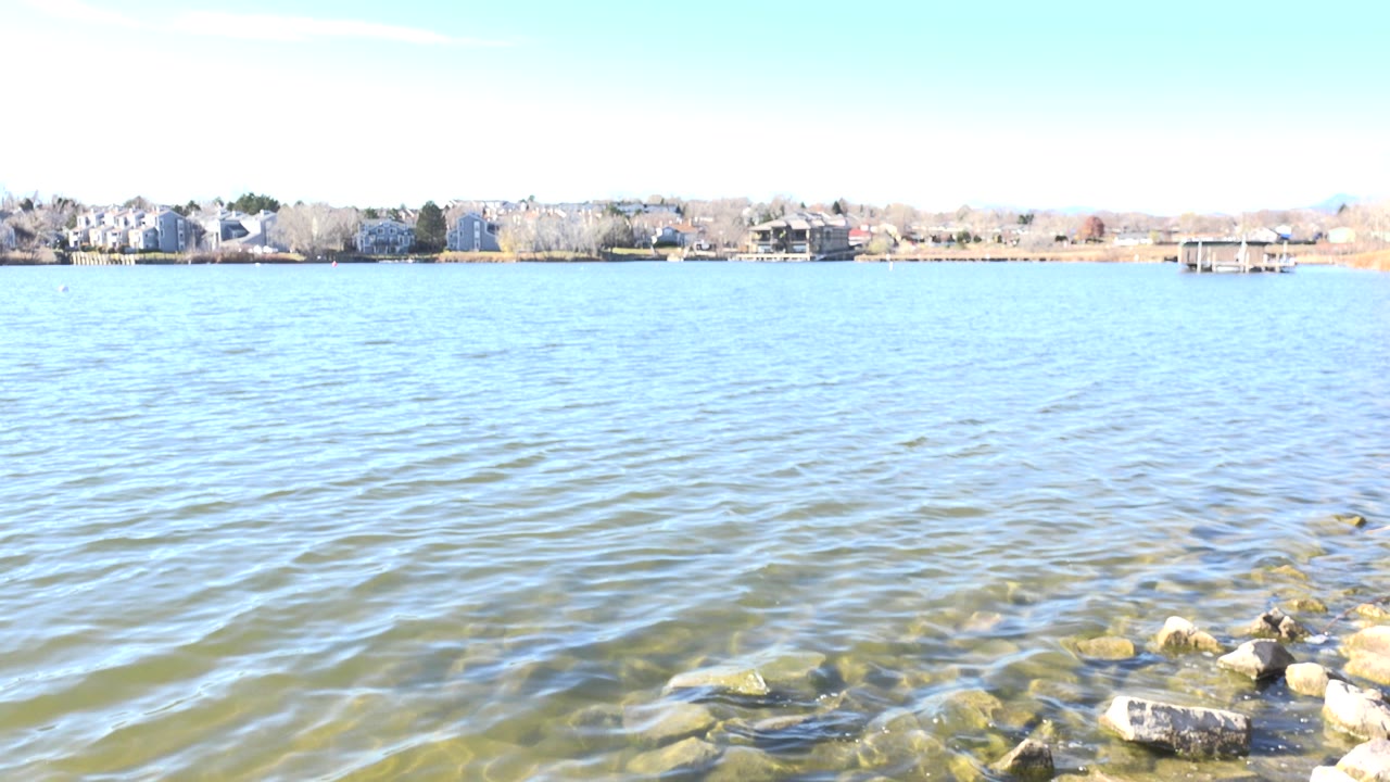 Rocky lake edge with rippled water and distant shoreline buildings