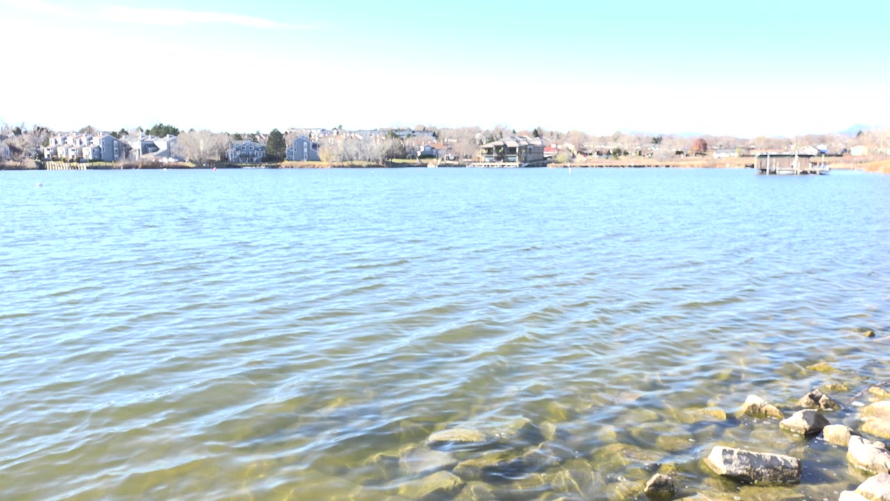 Wide bright water view with rocks at lower right and buildings on the far shore
