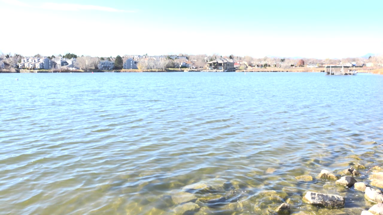 Opening frame of Hidden Lake, Colorado with bright rippled water, rocks at the lower right, distant homes and docks across the shore, and no visible people.