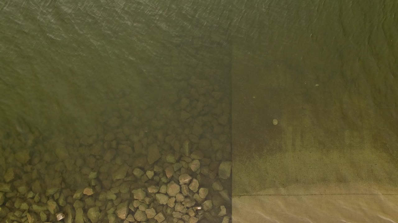 Overhead view in Jefferson County, Colorado showing clear green-brown water over rocks beside a pale riverbed edge, with no visible people.