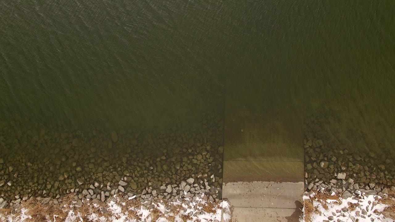 Overhead frame in Jefferson County, Colorado showing dark green water above a rocky, snow-dusted shoreline with no visible people.