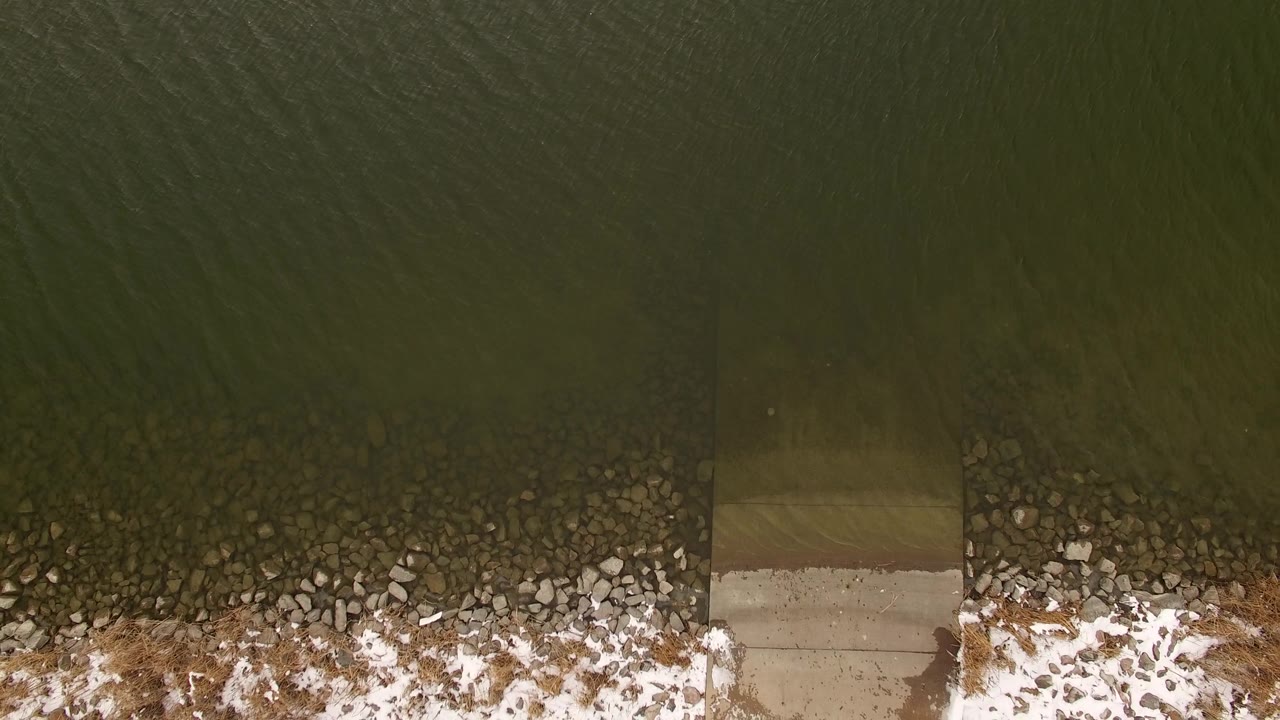 Dark water meets a rough shoreline with snow and scattered rocks