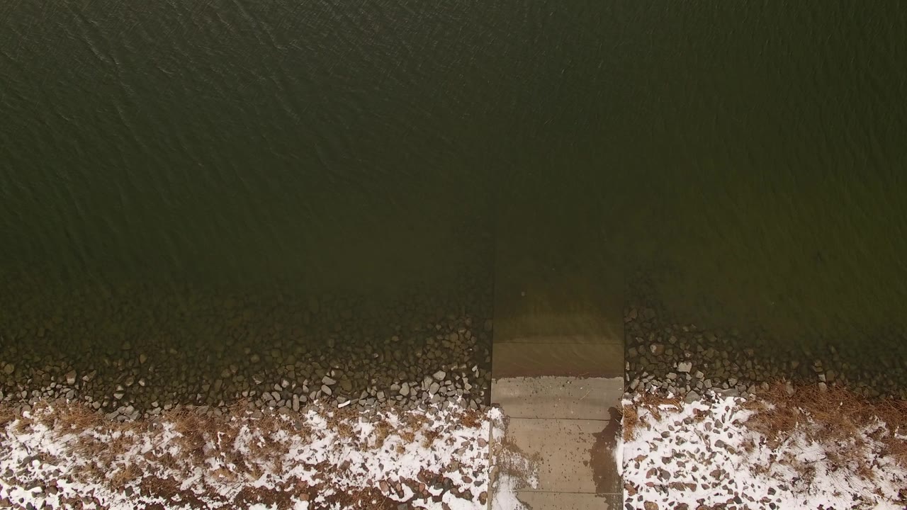 Overhead frame in Jefferson, Colorado showing dark green water, patchy snow along the bank, brown vegetation, and a concrete access edge with no visible people.