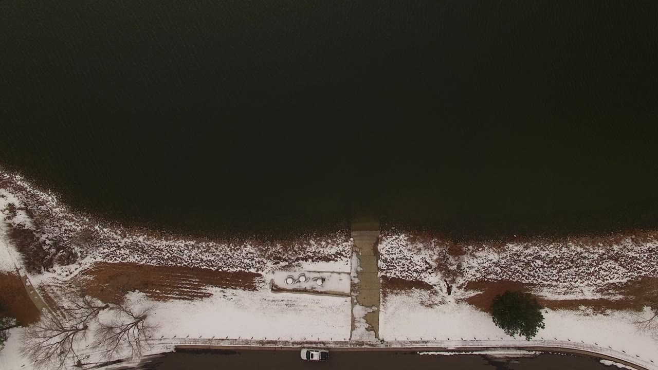 Jefferson County, Colorado overhead view with dark water across the top, snow-covered bank, a straight walkway to the shore, a small dock-like structure, road edge, and no visible people.
