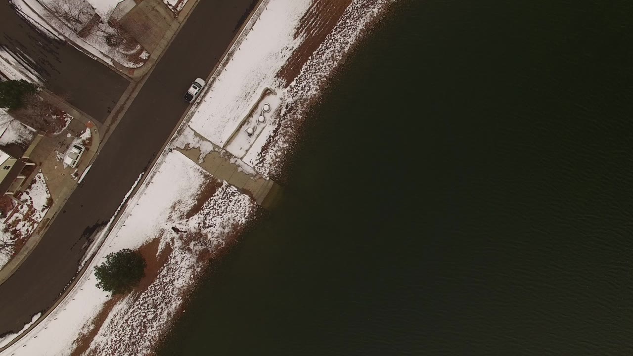 Overhead view of a snowy shoreline road beside dark water.