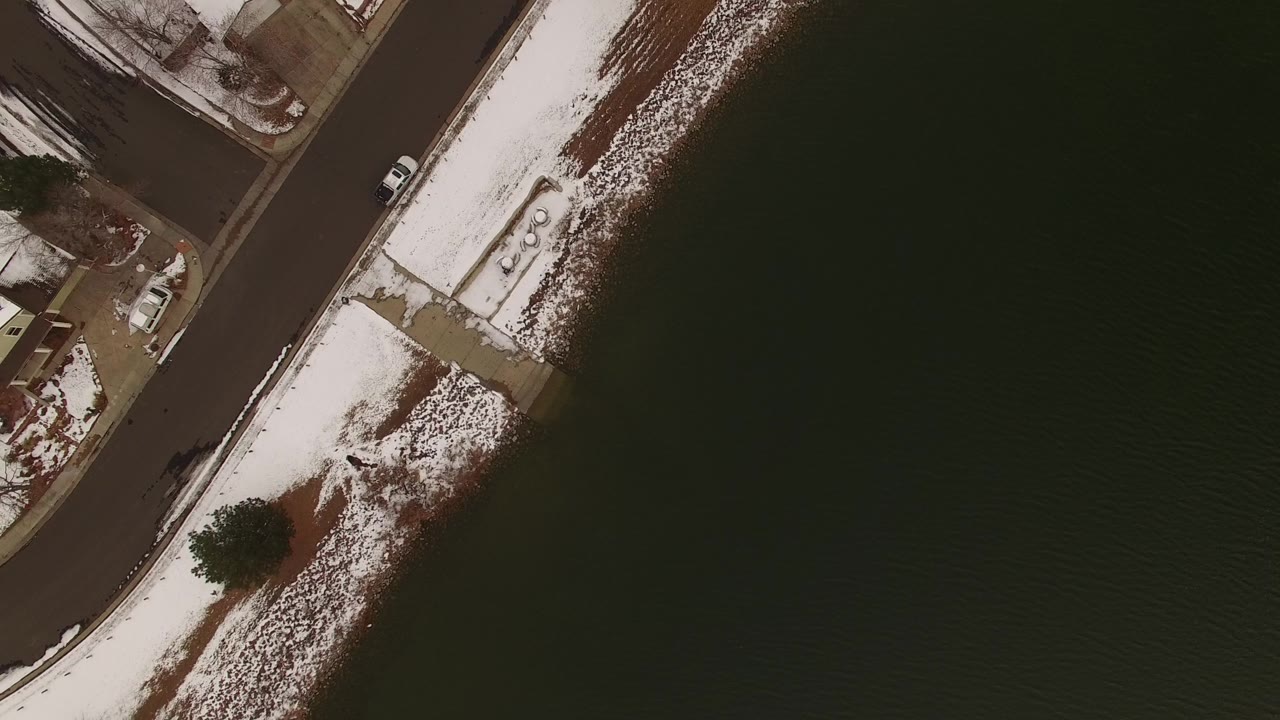 Overhead Jefferson, Colorado frame with a curved lakeside road, patchy snow, brown ground, a shoreline path, and no visible people.