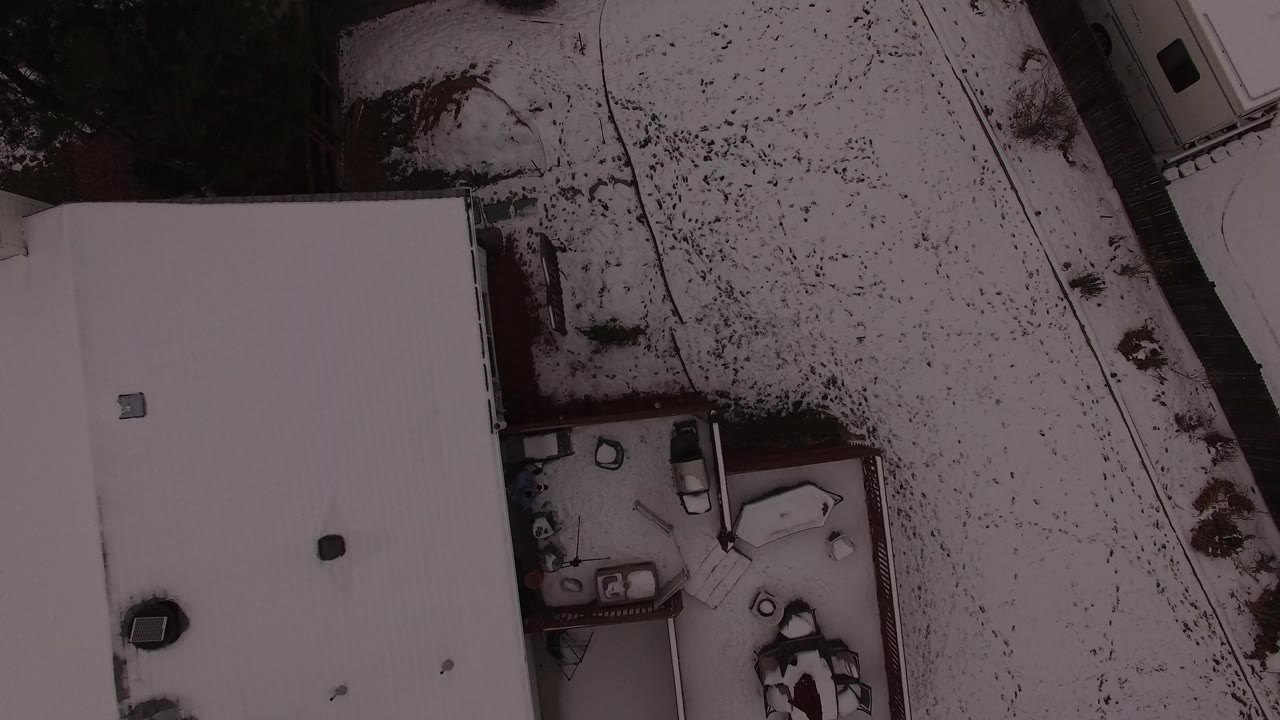 Overhead snowy roofs and residential yard beside a pale road